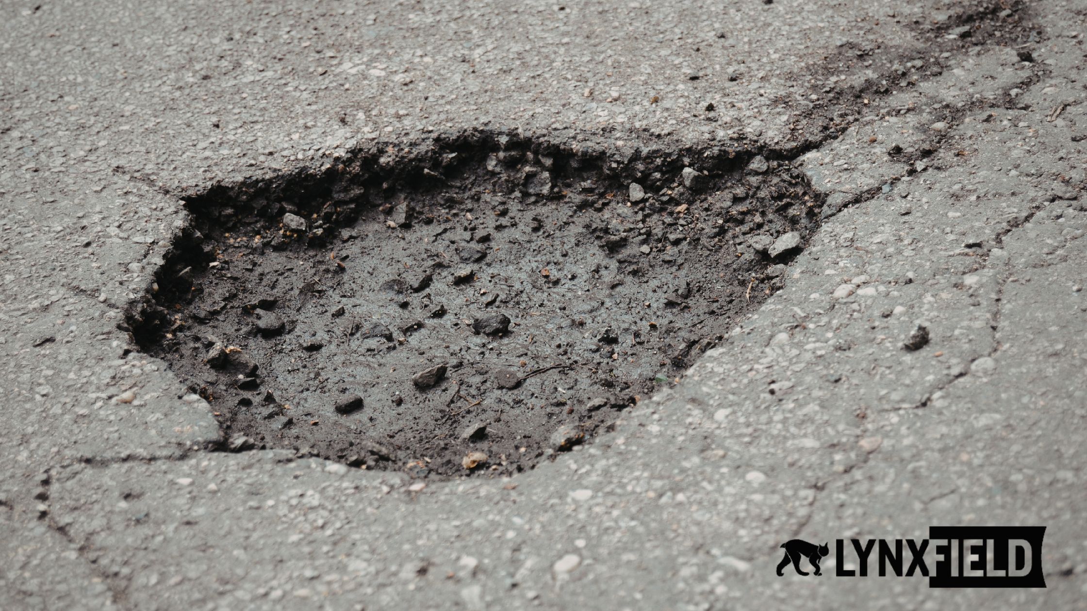 Large jagged pothole in cracked asphalt with loose stones