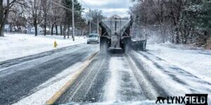 Municipal winter operations crew plowing and salting a roadway during a snowstorm, supported by automated reporting, fleet tracking, and salt usage documentation.